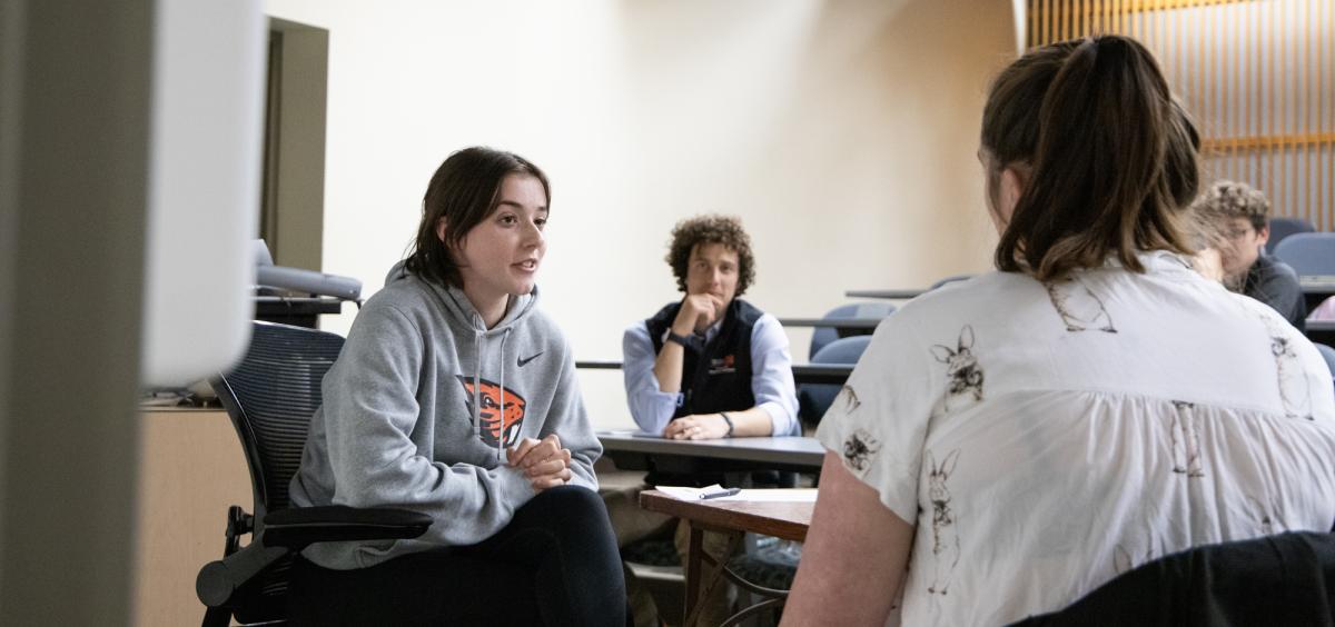 Two people talk in a classroom while another observes.