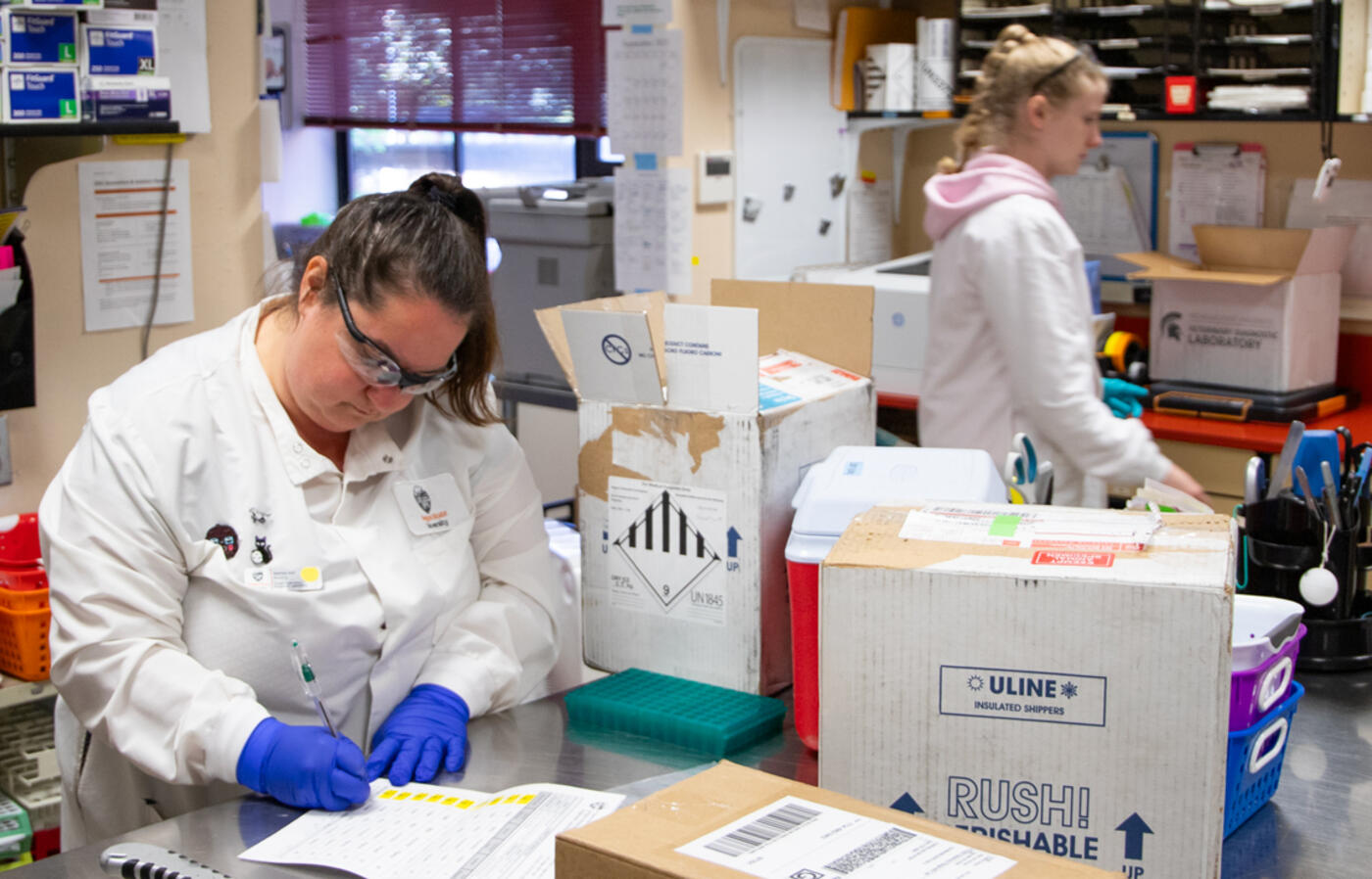 Three people open boxes and fill out accession forms in a receiving mail room.