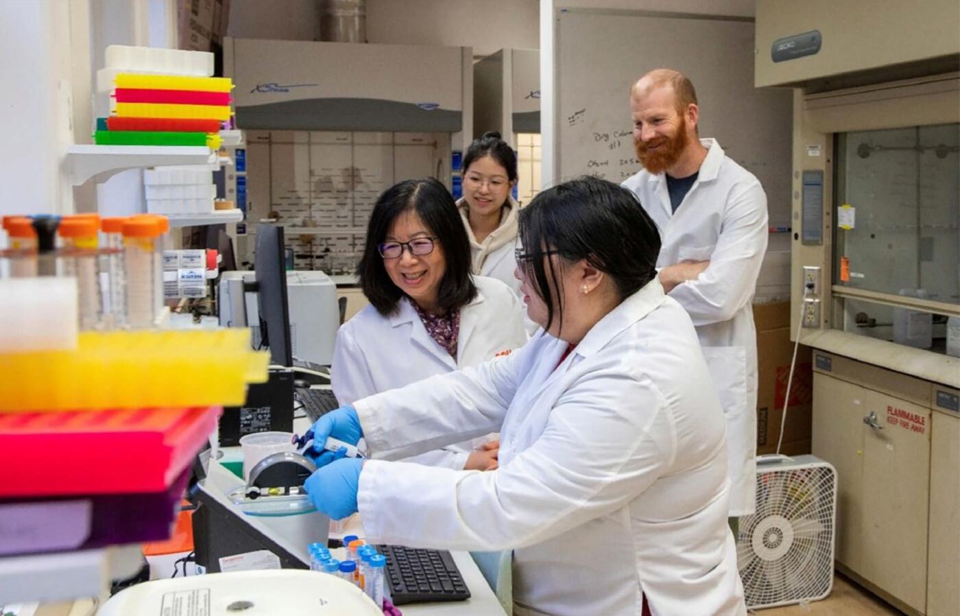 Four researchers in lab coats conduct an experiment in a laboratory.