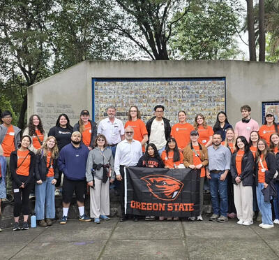 Group of people hold up Oregon State University flag with Beaver logo.