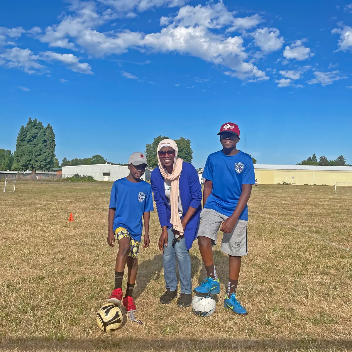Woman and two boys on a soccer field.