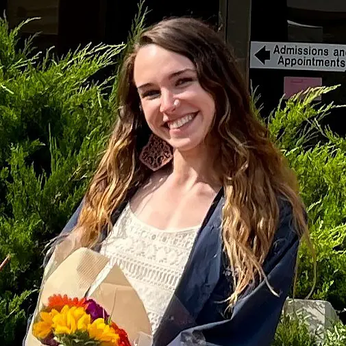 Woman in graduation robe stands outside.