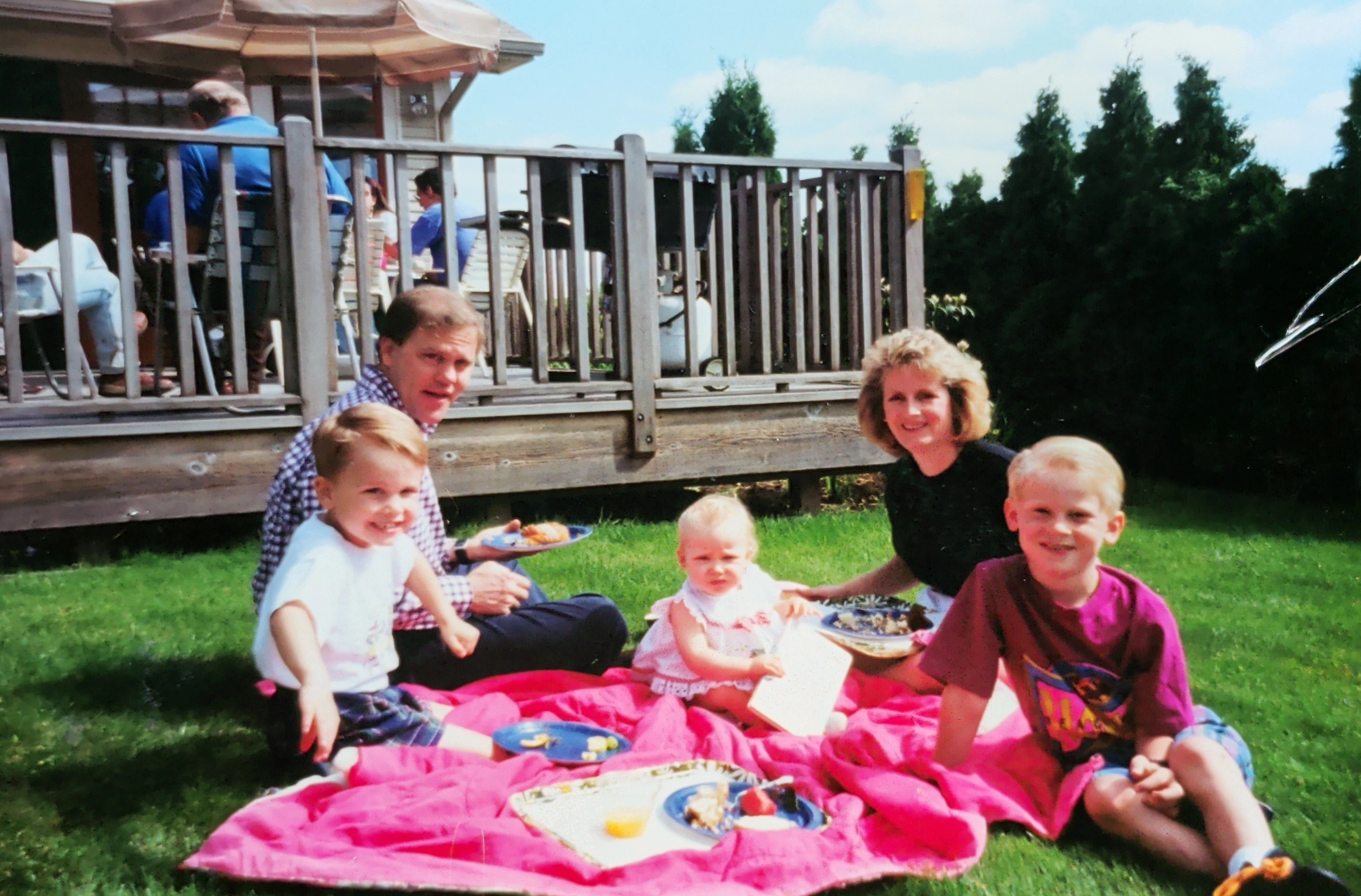 Family of 5 eating on a blanket in a backyard at a party. 