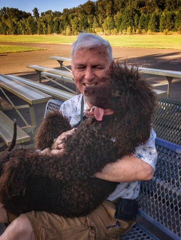 Large, fluffy, brown dog sitting on owners lap on a bench outside