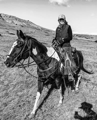 Black and white photo of a horse walking across grasslands with their owner sitting on their back 