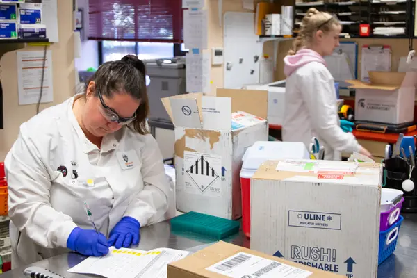 Three people open boxes and fill out accession forms in a receiving mail room.