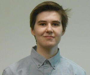 Person smiling in front of a blank wall and wearing a collared shirt