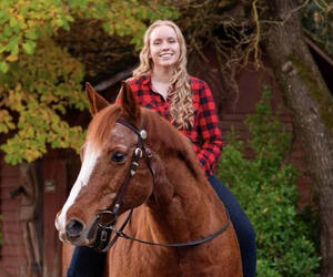 Woman sits on horse with barn in background.