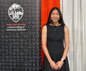 Woman stands next to banner that says Oregon State University Carlson College of Veterinary Medicine.