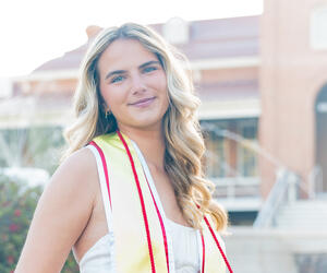 Woman in white dress with graduation cord and sash.